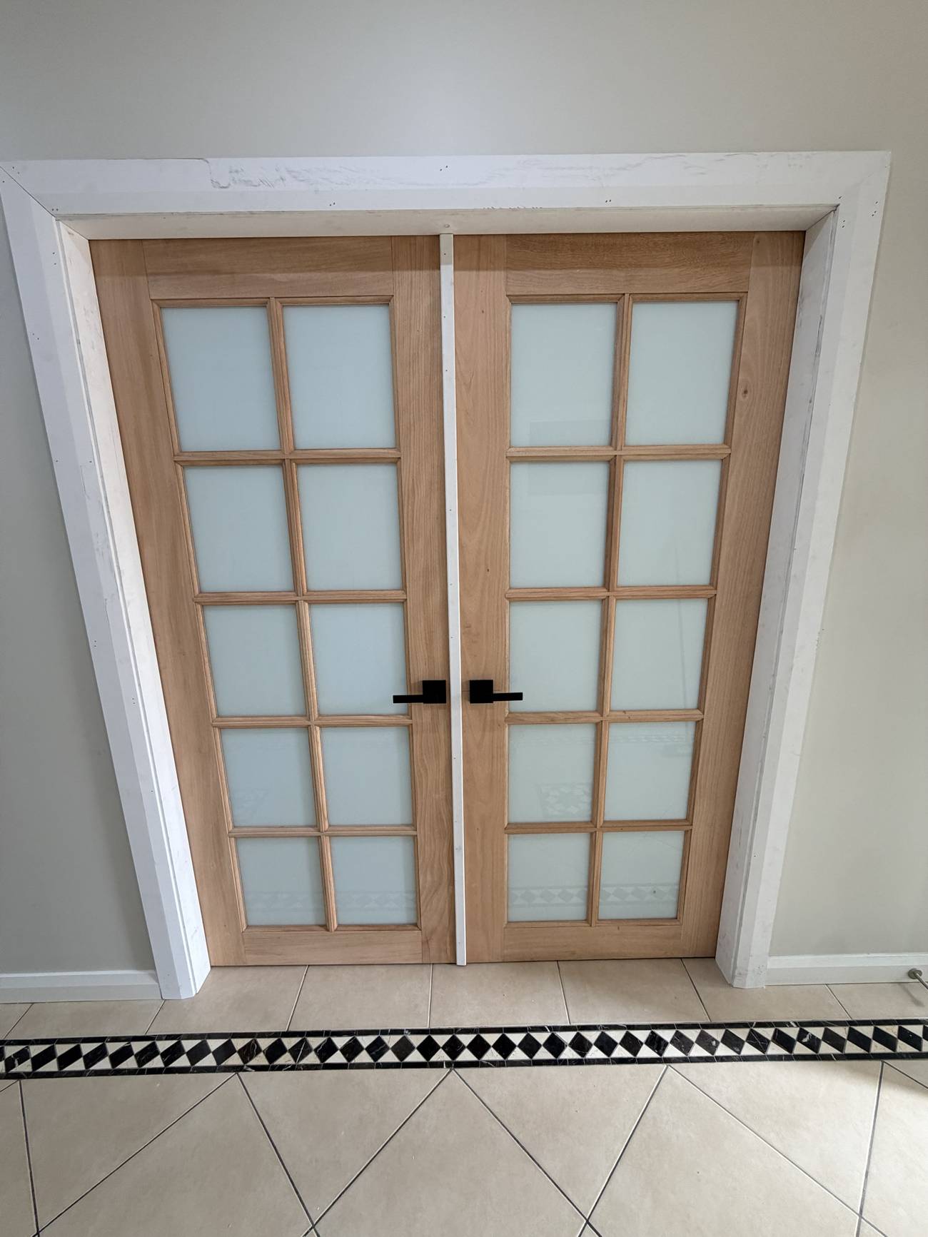 Pair of timber French doors with frosted glass and black lever handles, newly installed