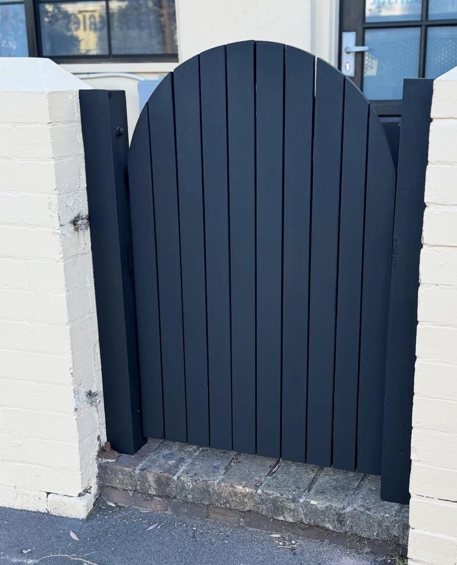 New arched timber gate painted black between rendered brick pillars